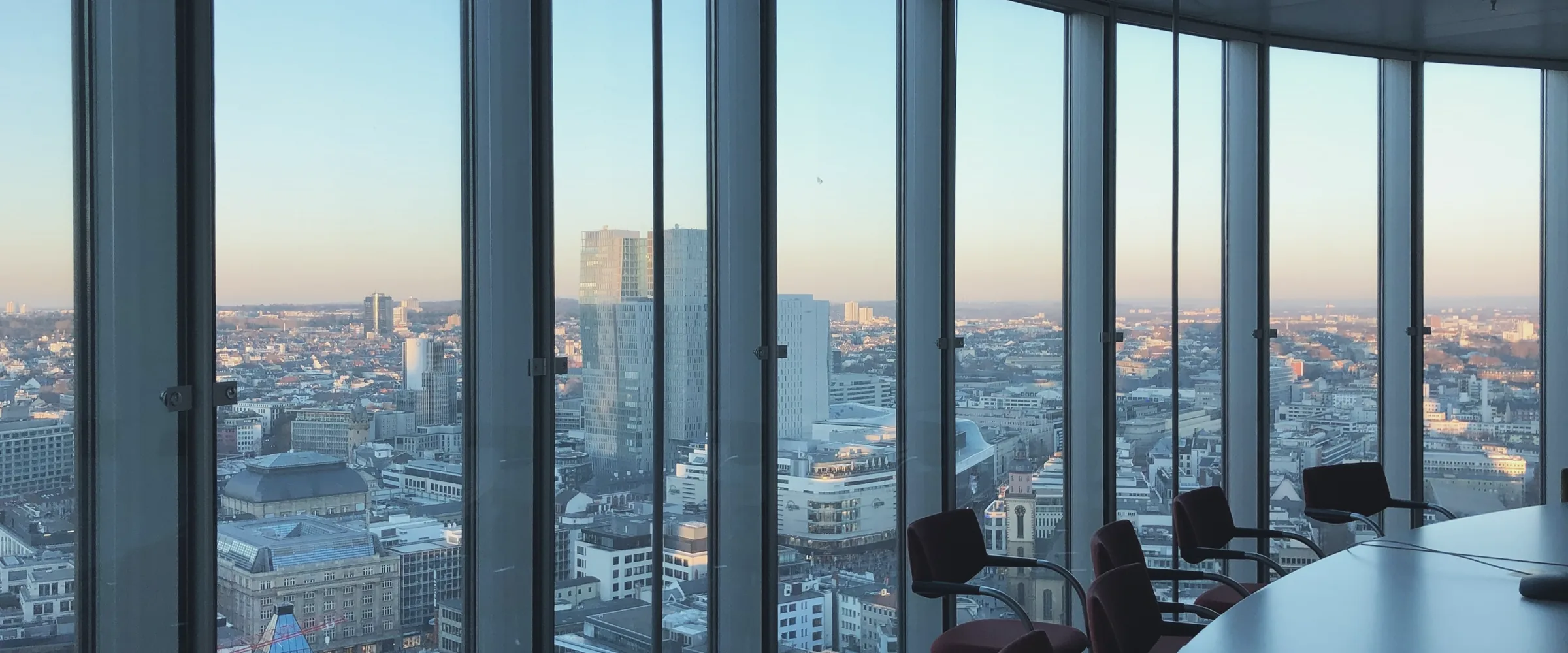 A curved glass wall on a high floor at dusk, looking out over a city.